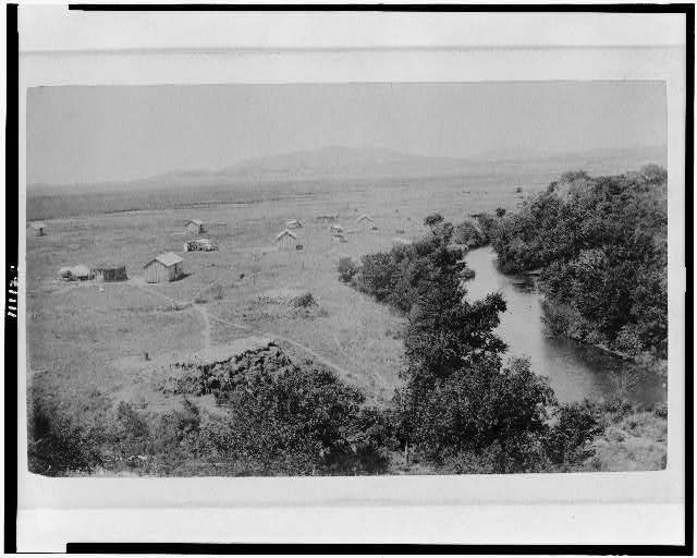 [Bird's-eye view of rural buildings and creek or river,...