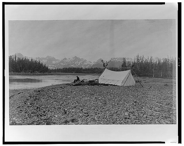 [A man, possibly B.E. Fernow, seated next to river, tent...