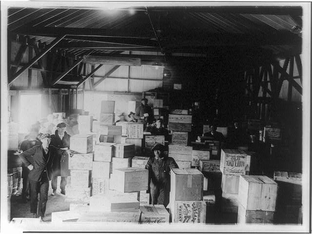 [Men standing in warehouse with cases of confiscated(?)...