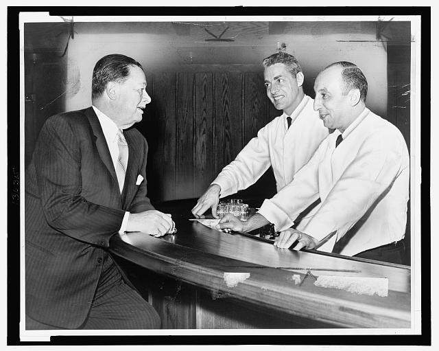 Toots Shor, left, passes the word to his bartenders, Bob...