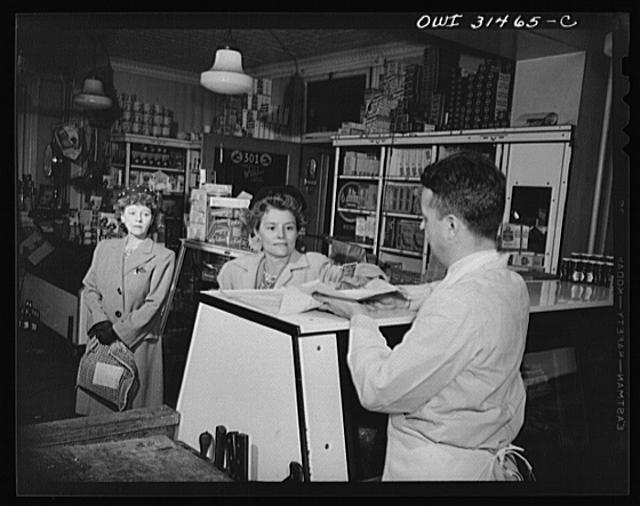 Two women and a butcher at a meat counter, in a scene...
