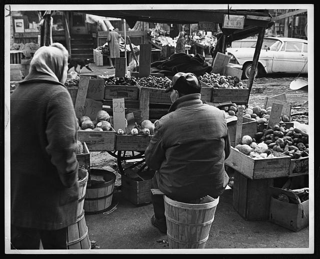 [Produce vendor, bundled up against the cold, sits on a...