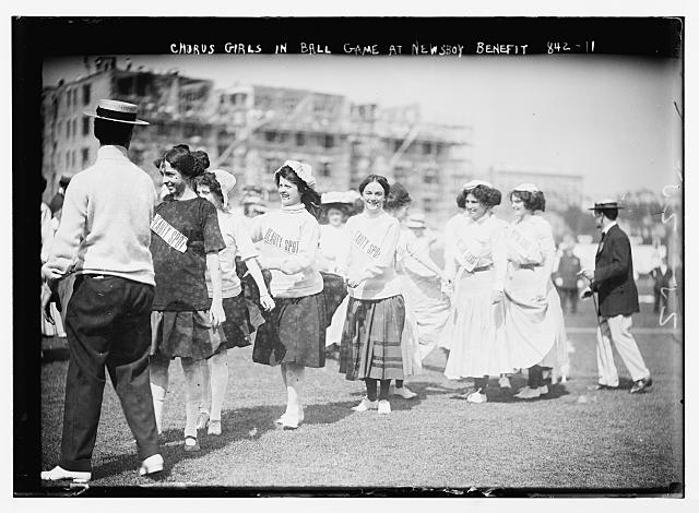Chorus girls lined up on playing field in ball game for...