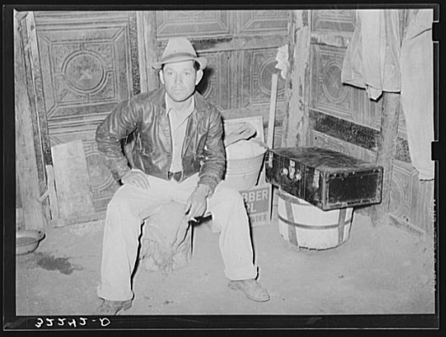 Mexican man in corner of one-room dwelling. Notice dirt...