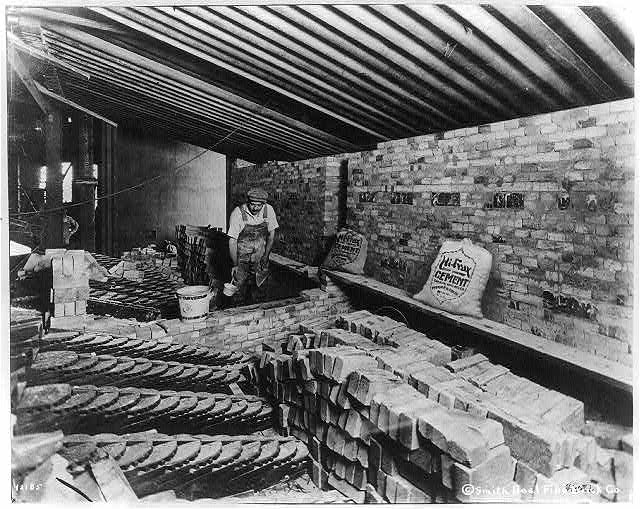 [Man laying bricks inside building]