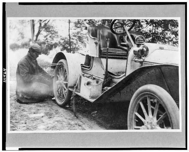 [Man fixing tire on a Buick roadster outside of Liberty,...
