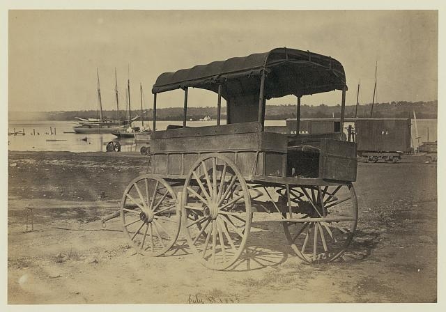 [Covered wagon with side curtains rolled up at a military...