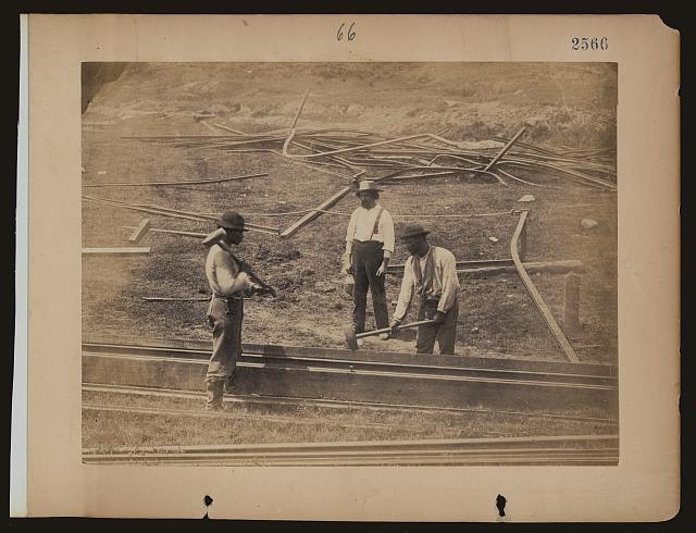 [Two railroad construction workers hammer track as third...