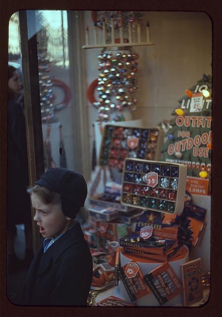 [Boy beside store window display of Christmas ornaments]