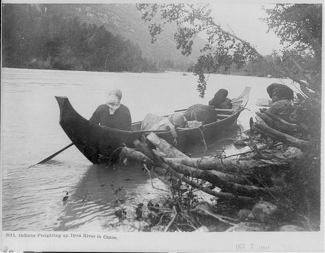 Indians [2 women and child] freighting up Dyea River in...