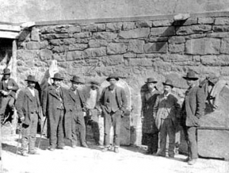Photo taken in front of the Old Town Jail in Las Vegas, New Mexico. John Joshua Webb is shown here, with his feet shackled, in the center of the photo.
