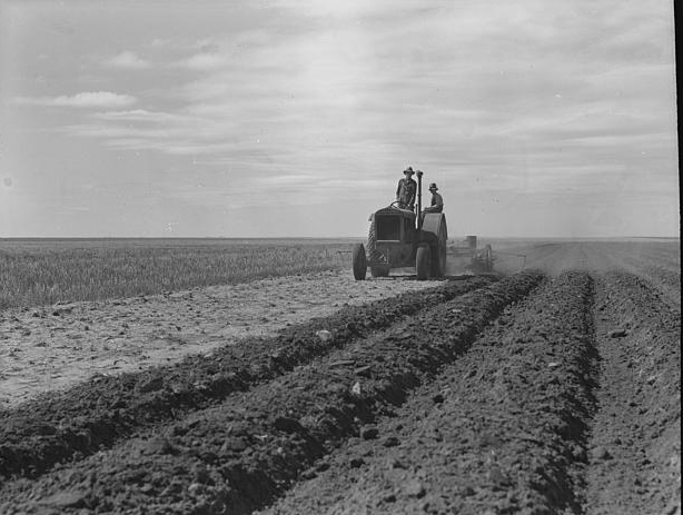 Dust bowl farmer driving tractor with young son near...