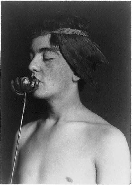 [Boy in headband, shirtless, holding metal "poppy" to...