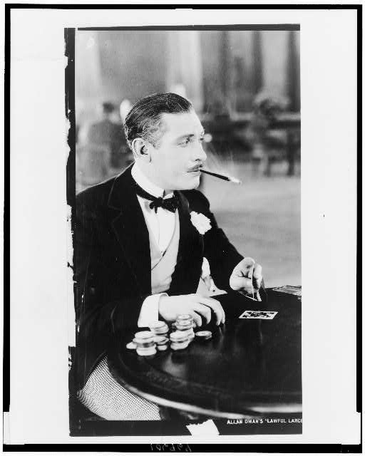 [Man, with cigarette holder in mouth, playing cards]