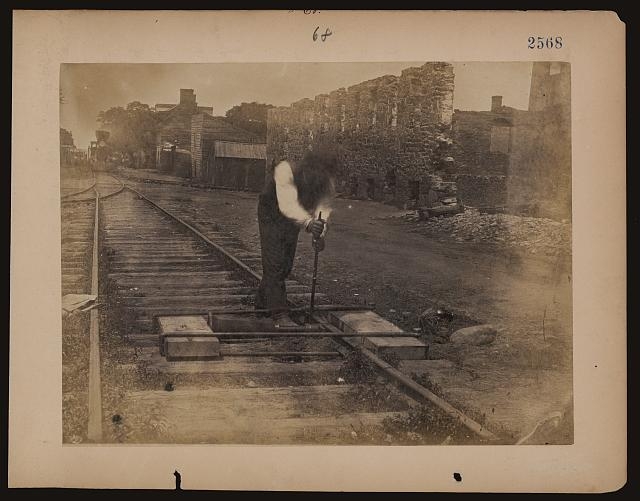 [Railroad construction worker straightening track]