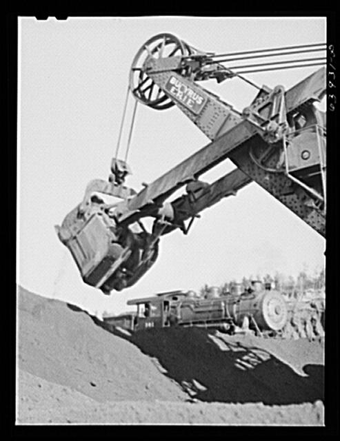 Electric shovel loading iron ore into railroad cars,...