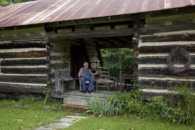 John Herbert weaves baskets in a dogtrot log cabin,...