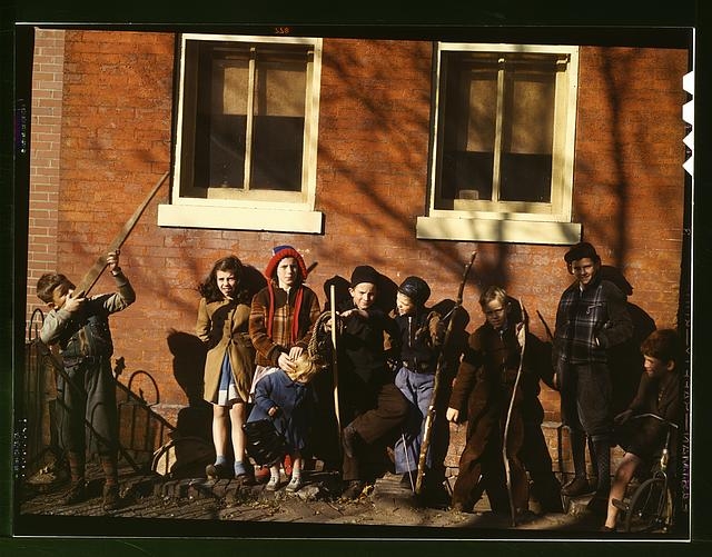 [Children aiming sticks as guns, lined up against a brick...