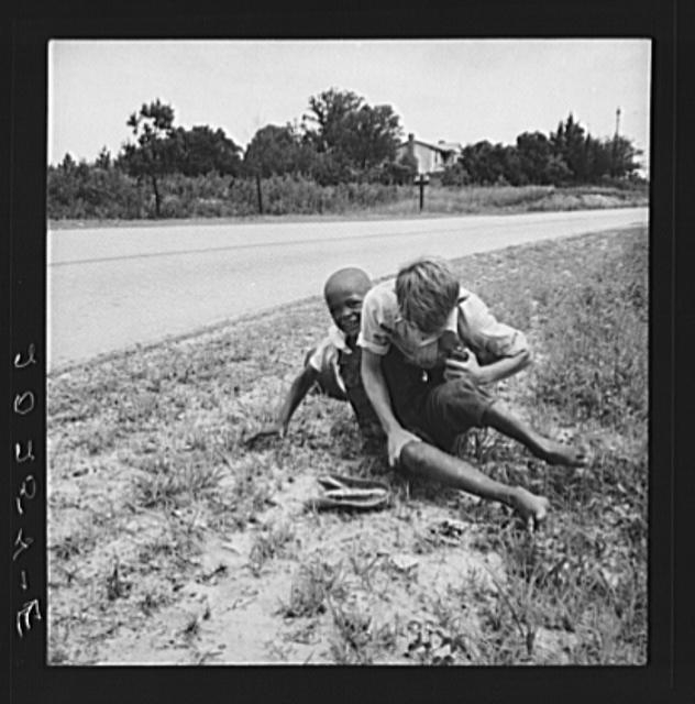 White and Negro boy wrestling by side of road. Person...
