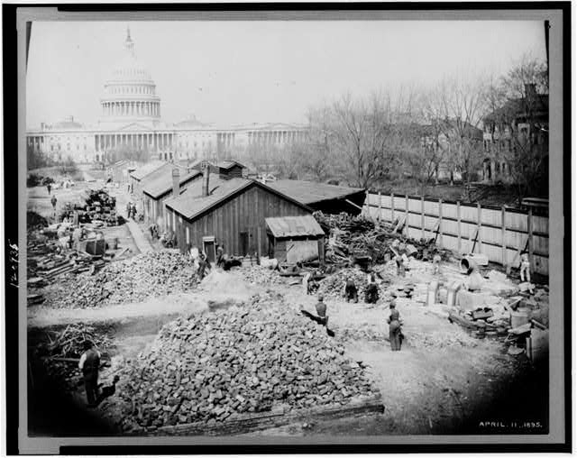 [Sheds, piles of bricks and workers during construction...