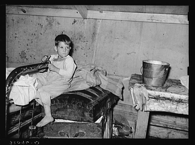 Son of white migrants sitting on trunk in tent home....