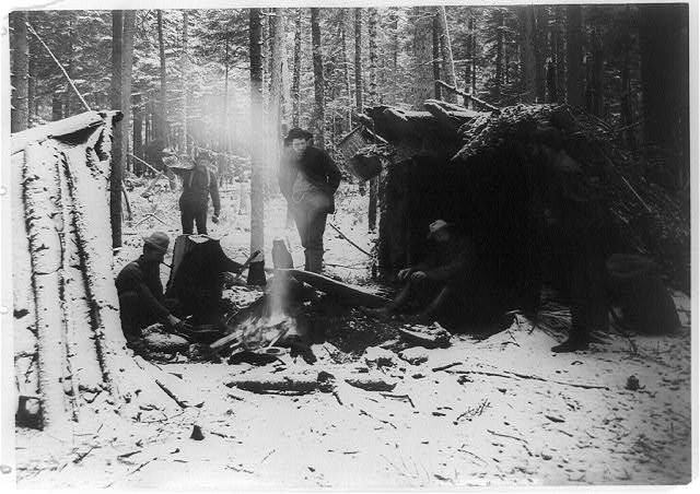 [Five men at campfire in camp in the Adirondacks in winter]