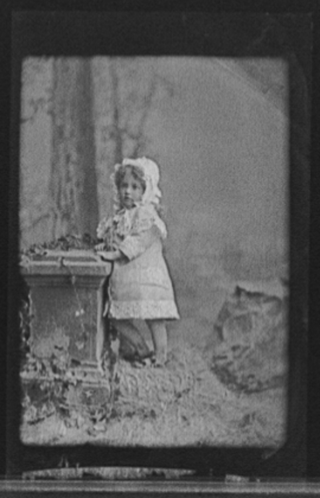 [Girl in cap posed by stone monument]