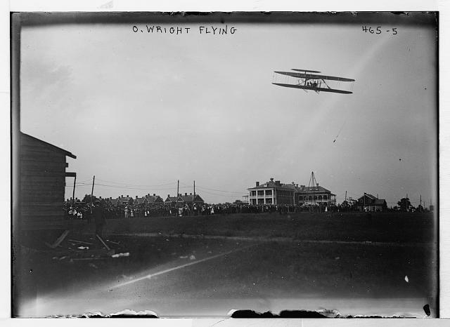 O. Wright flying in his airplane, crowd on field