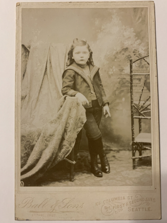 Young child with long curls wearing pants. Photo taken by Ball and Sons. Seattle, Washington. 