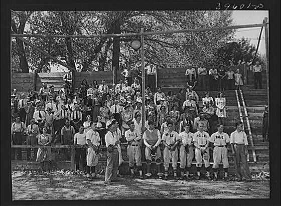 Baseball players and spectators stand at attention while...
