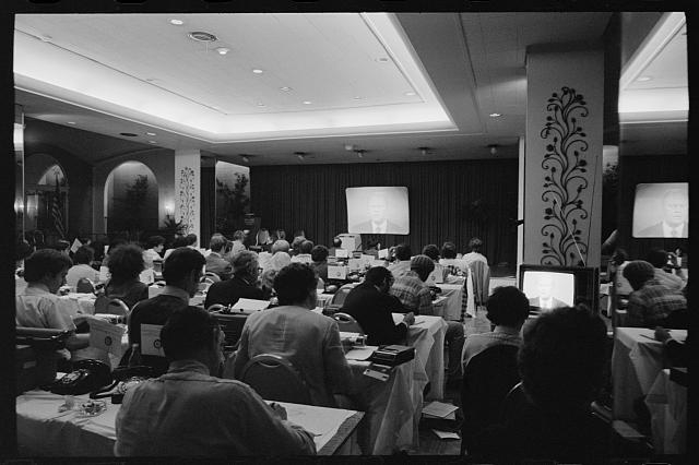 [Reporters in press room observe President Gerald Ford on...