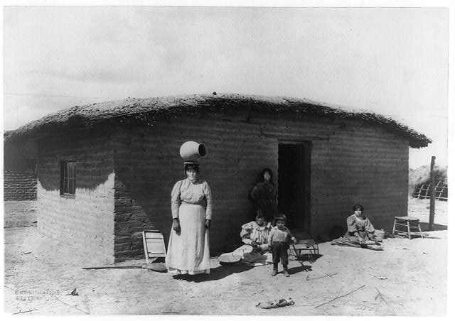 [Five Pima Indians posed outside adobe house--one woman...