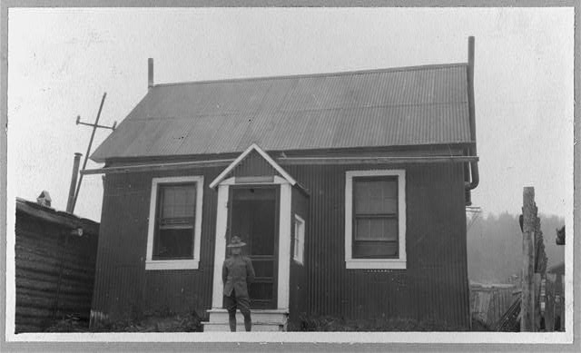 [Uniformed man in front of house, Yukon River area]
